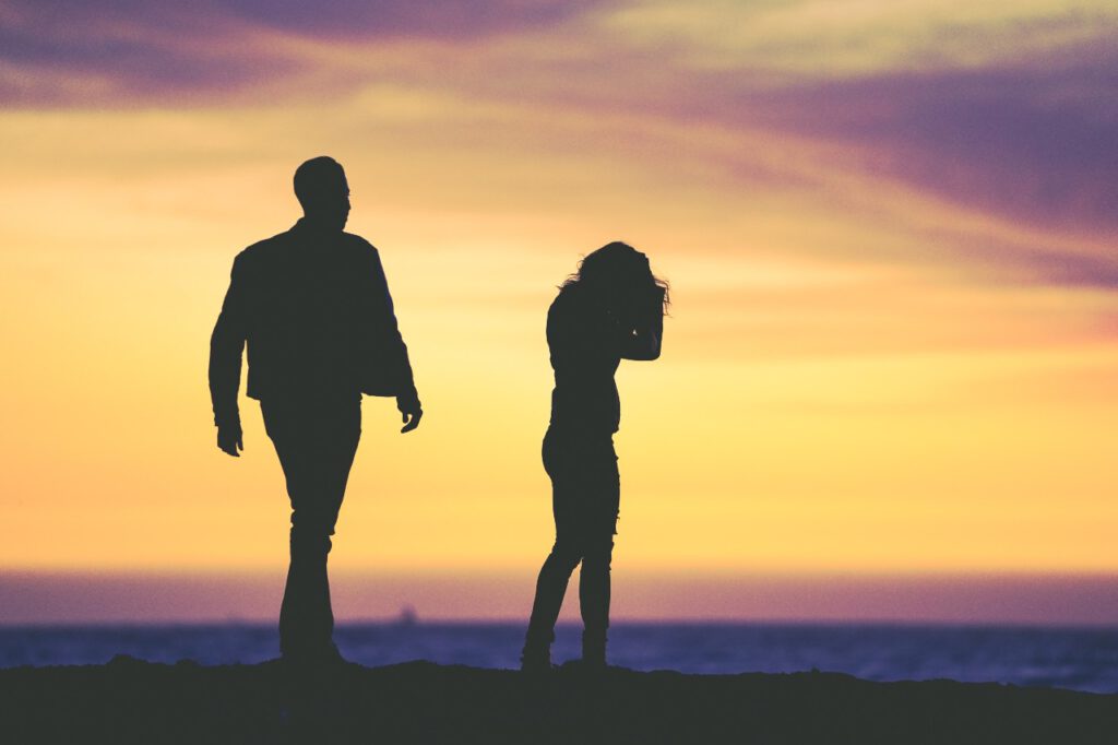 Man and woman fighting in the sunset, it's unclear whether he is walking away from her or towards her to comfort her.