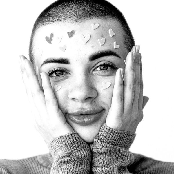 A black and white portait of a woman cupping her face, covered with heart stickers.