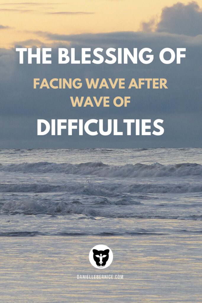 A photograph of waves coming in from the sea onto the shore. While the clouds up ahead are dark and ominous, there is a bright orange sky above the clouds, promising better weather. The text reads: The blessing of facing wave after wave of difficulties. DanielleBernice.com.
