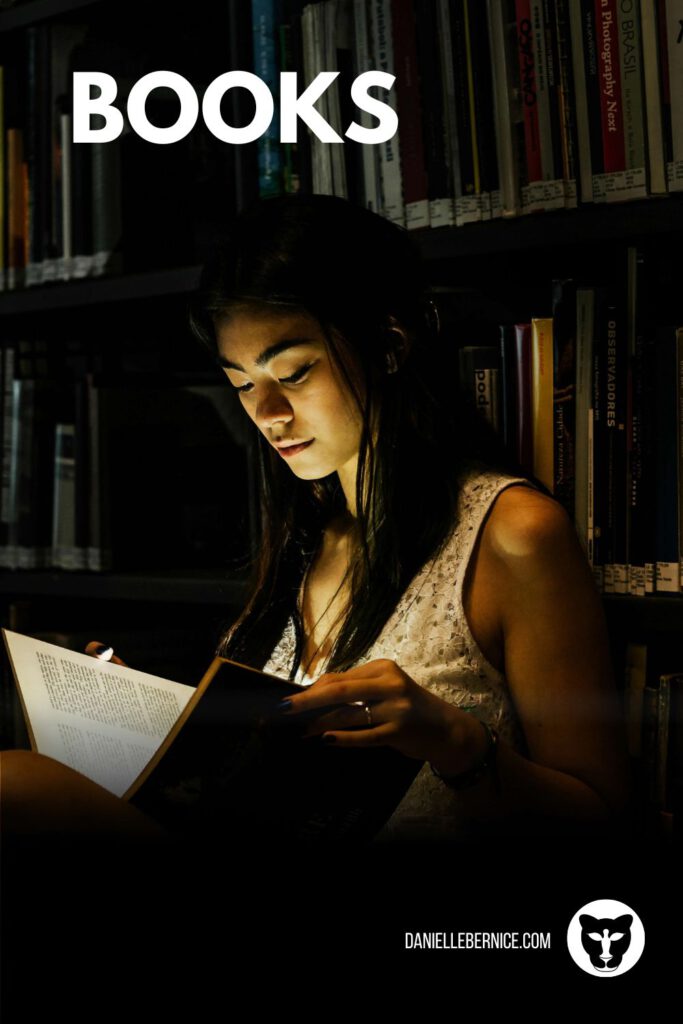Woman sitting in dark library reading a book that emanates light and illuminates her face. Text overlay says: Books, DanielleBernice.com