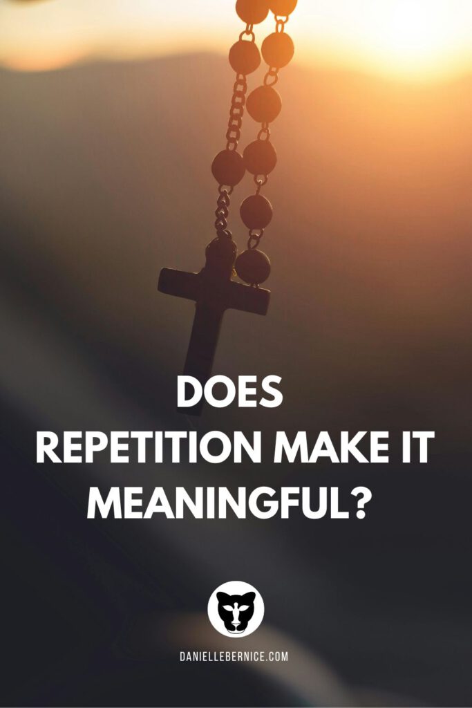 An image of a rosary hanging from the rear view mirror with the sunset over the mountains in the background. The text reads: Does repetition make it meaningful? DanielleBernice.com