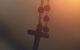 An image of a rosary hanging from the rear view mirror with the sunset over the mountains in the background.