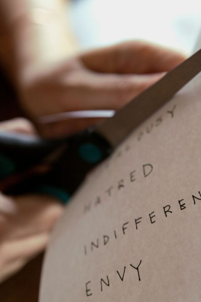 Photo of a woman's hands cutting a piece of paper with the words "hatred," "indifference," and, "envy."