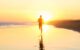 A photo of a man running on the beach towards the sunrise, leaving footsteps in the wet sand.