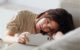 Photo of a tired woman resting her head on the couch while looking at her phone.